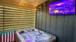 Ein moderner Spa-Bereich mit Holzboden, einer Whirlwanne, einem Flachbildfernseher und einem gemusterten Boden.