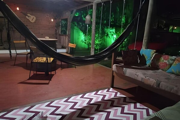 A hammock chair, a sofa, and a table in a room with a patterned rug. - One-Bedroom Suite (Paraty)
