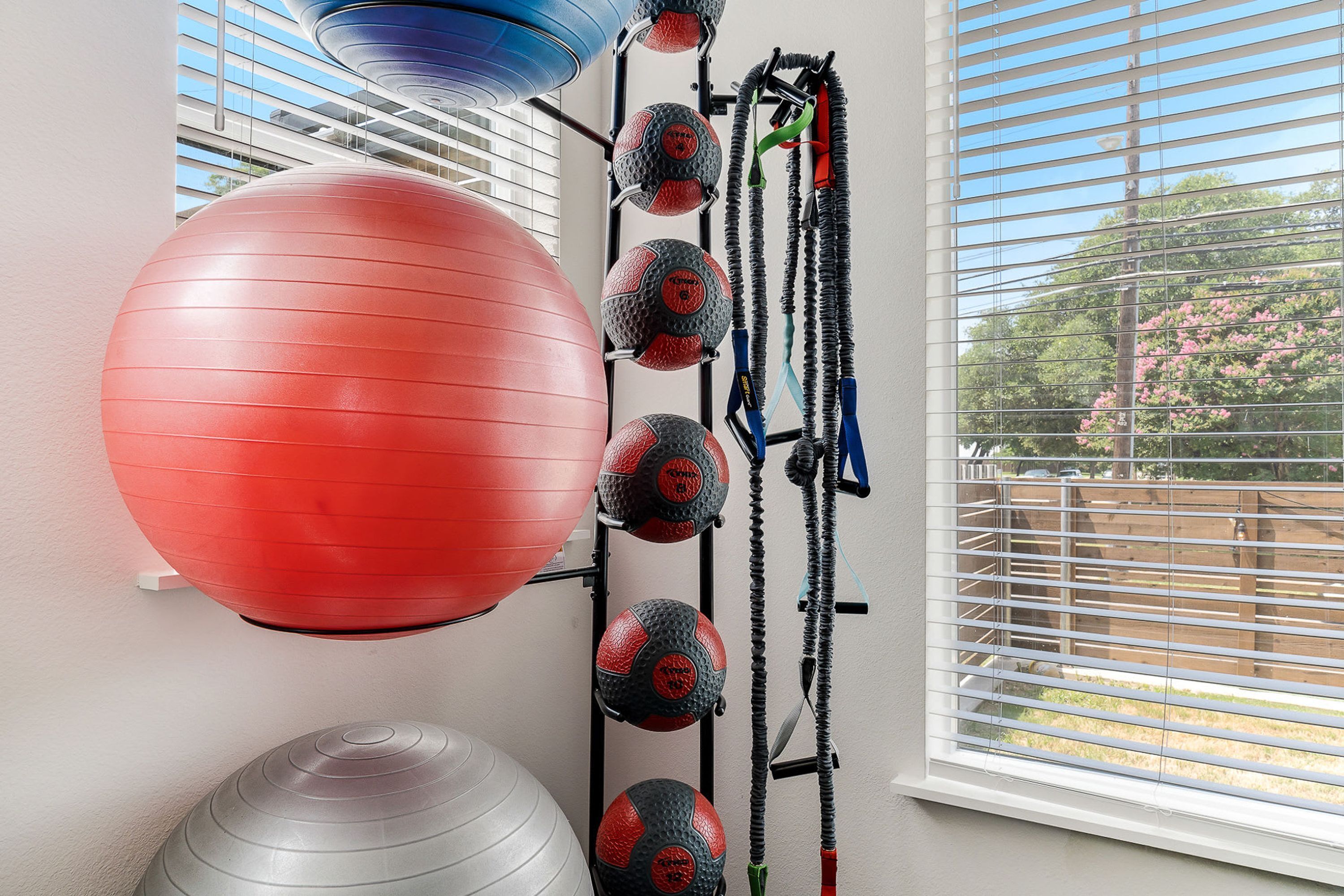 Une salle de sport équipée de matériel d’exercice, notamment un grand ballon rouge, des ballons de musculation plus petits, rouges et noirs, et des bandes de résistance.