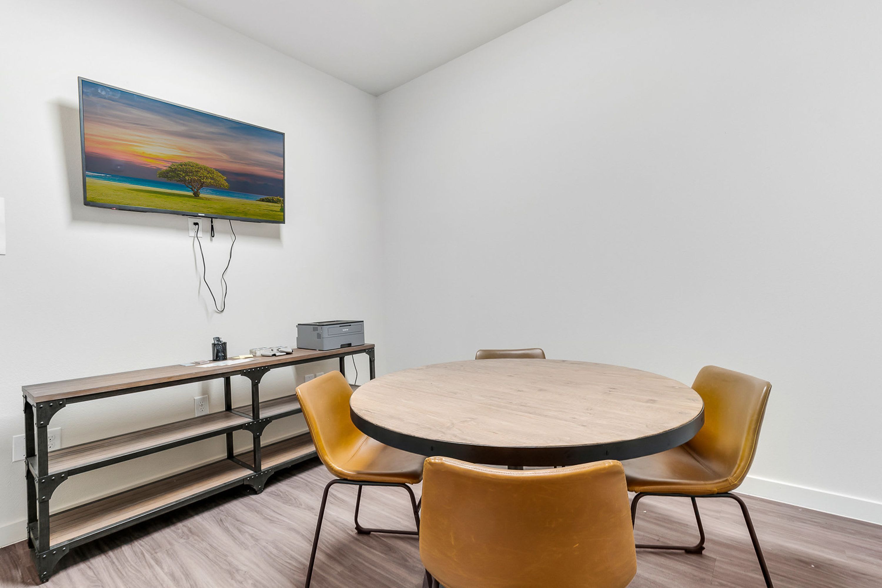 A conference room with a round table, four chairs, a bench, and a painting on the wall.