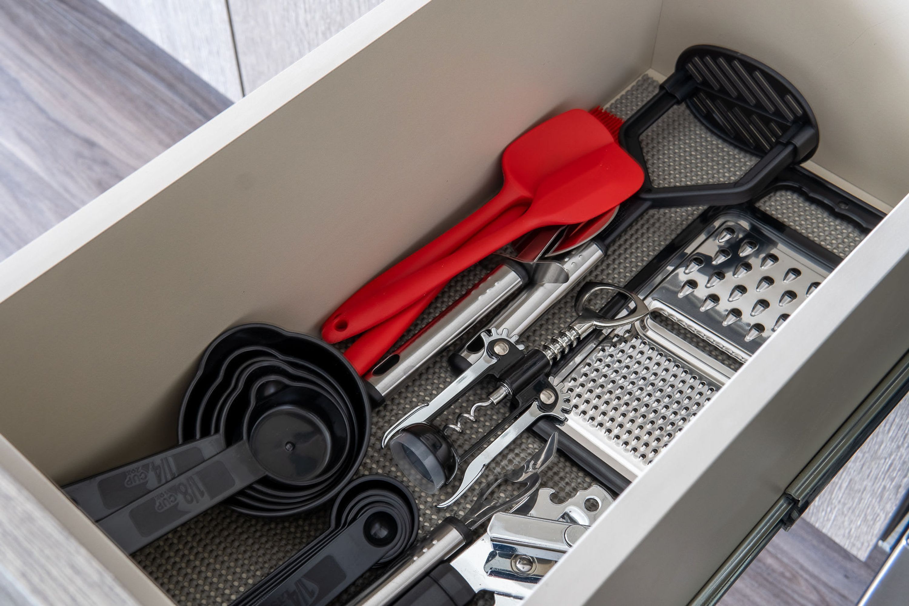 A drawer with various kitchen utensils, including a red spatula, black spatula, and a grater.