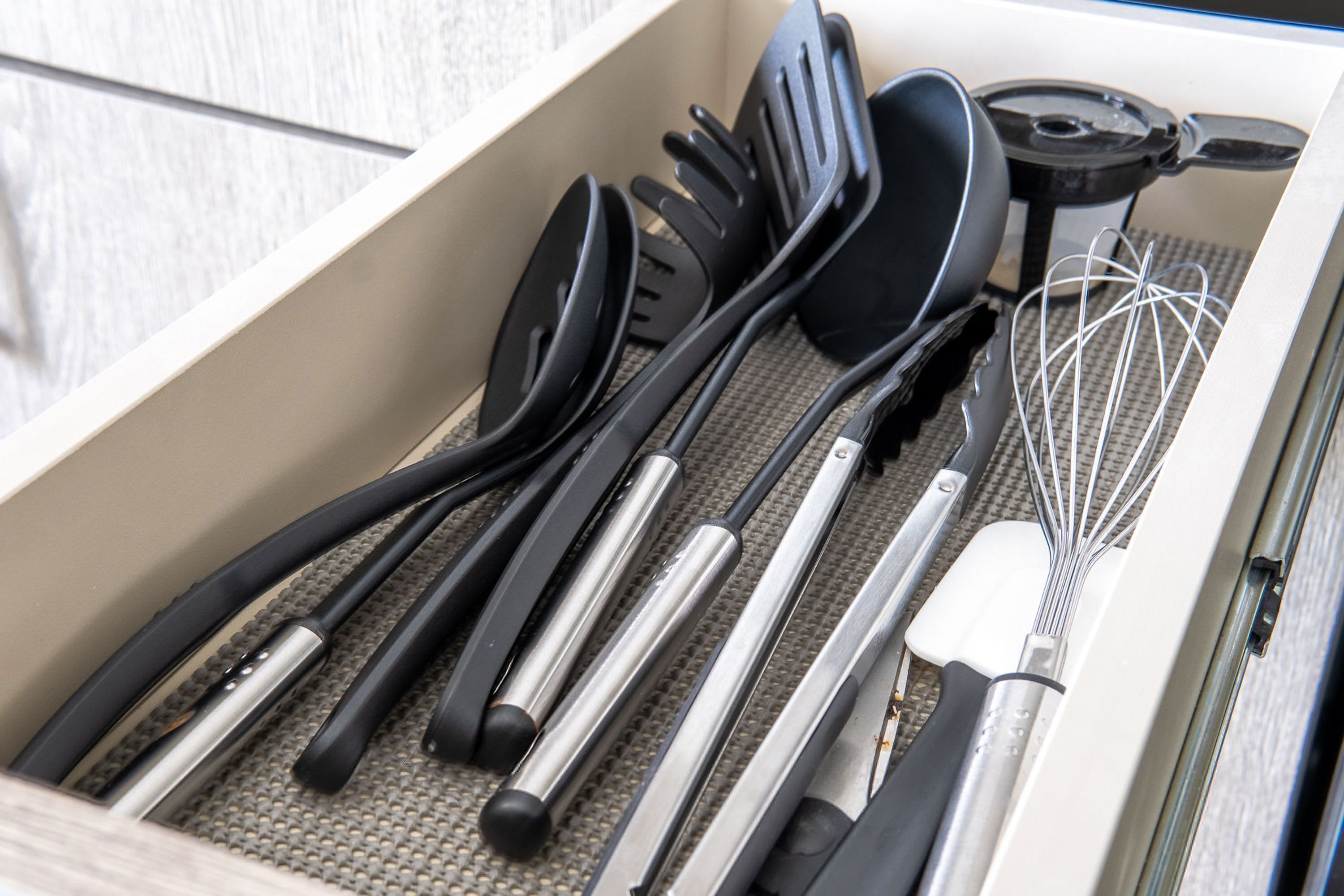 A drawer containing various kitchen utensils including spatulas, tongs, and a whisk.