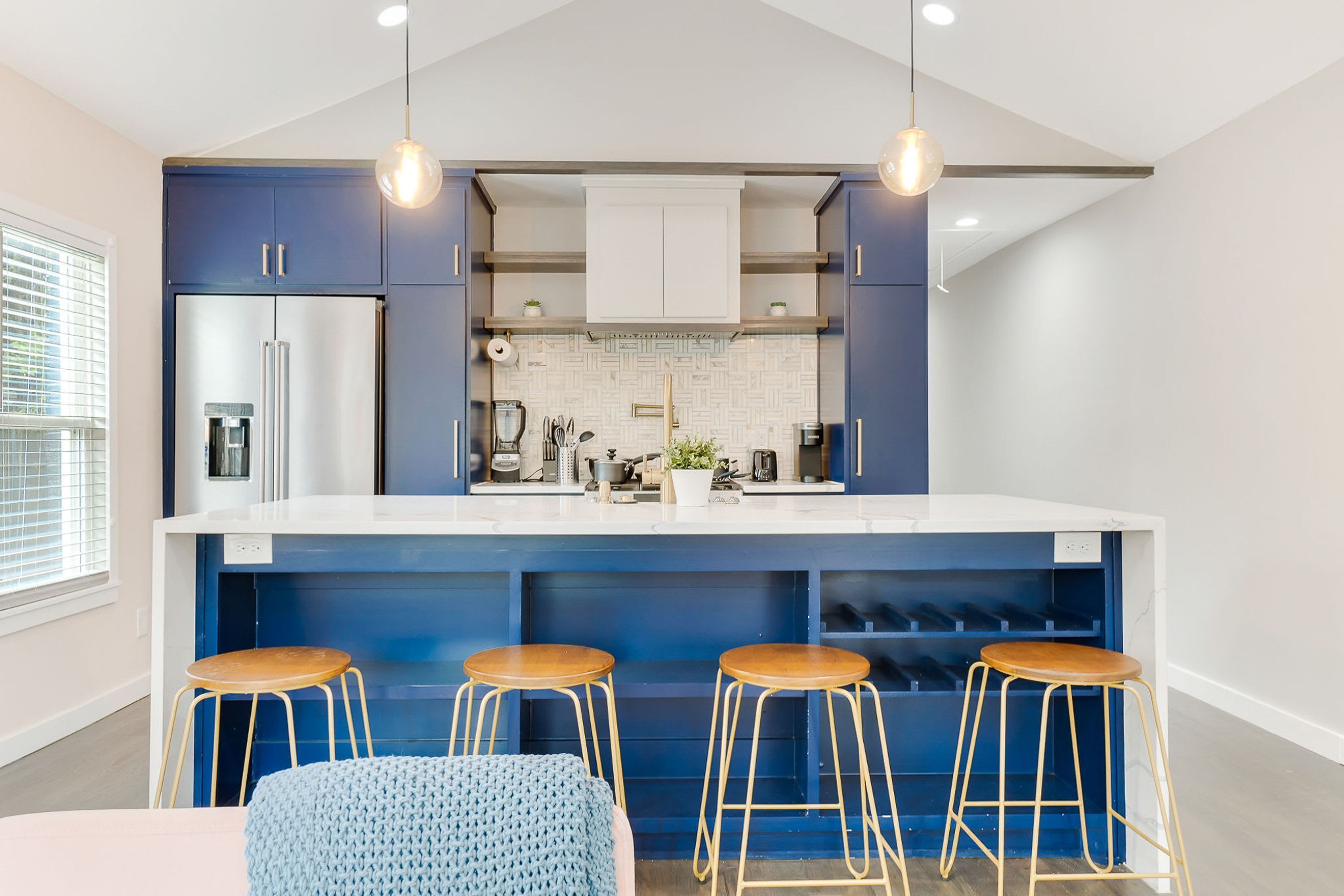 A modern kitchen with a central island, bar stools, and pendant lighting.