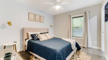 Une chambre à coucher avec un lit, un ventilateur de plafond, une fenêtre avec des rideaux et une petite table sur laquelle se trouve un plateau.