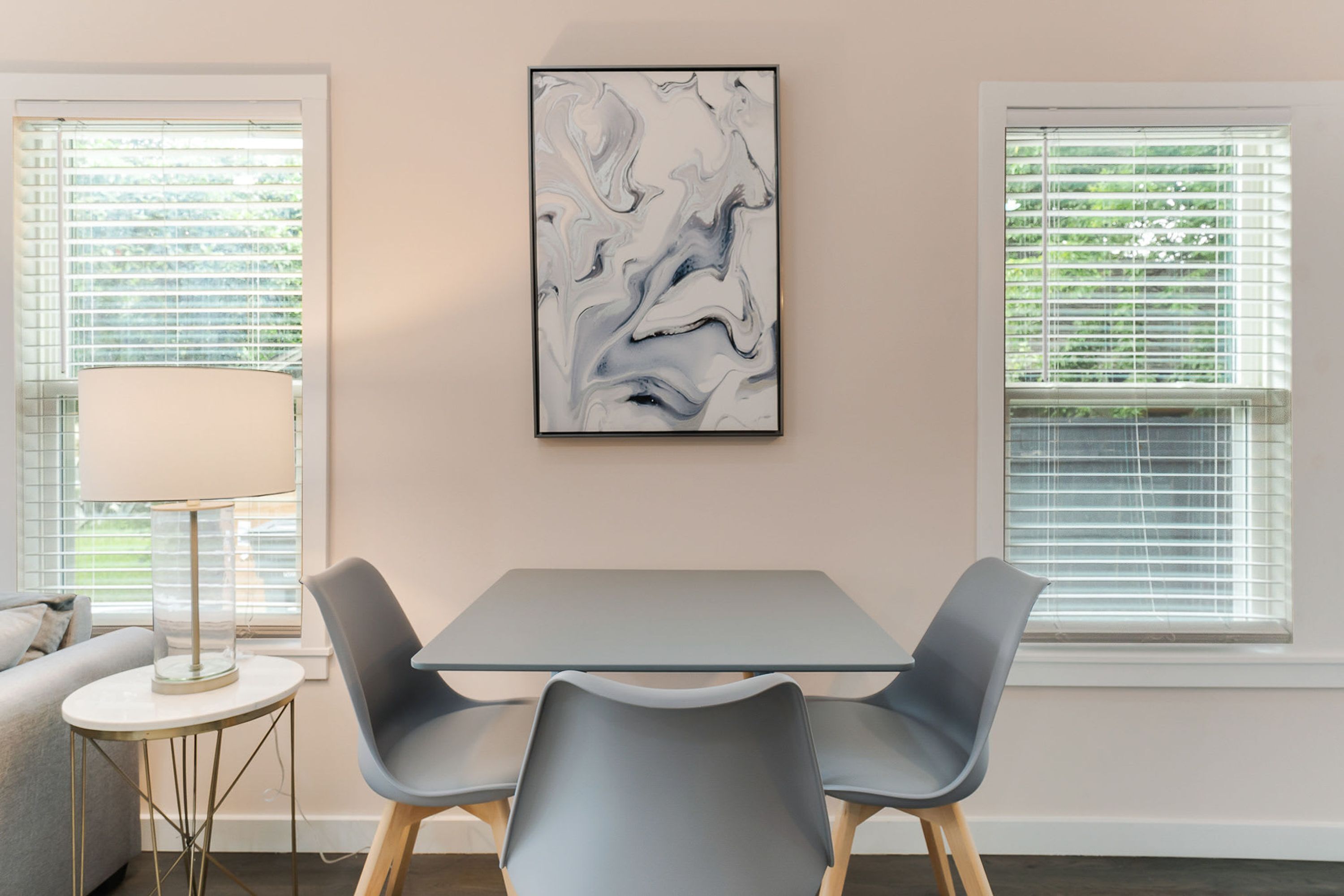 Un espace de salle à manger moderne avec une table et des chaises, une lampe et un tableau abstrait encadré accroché au mur.