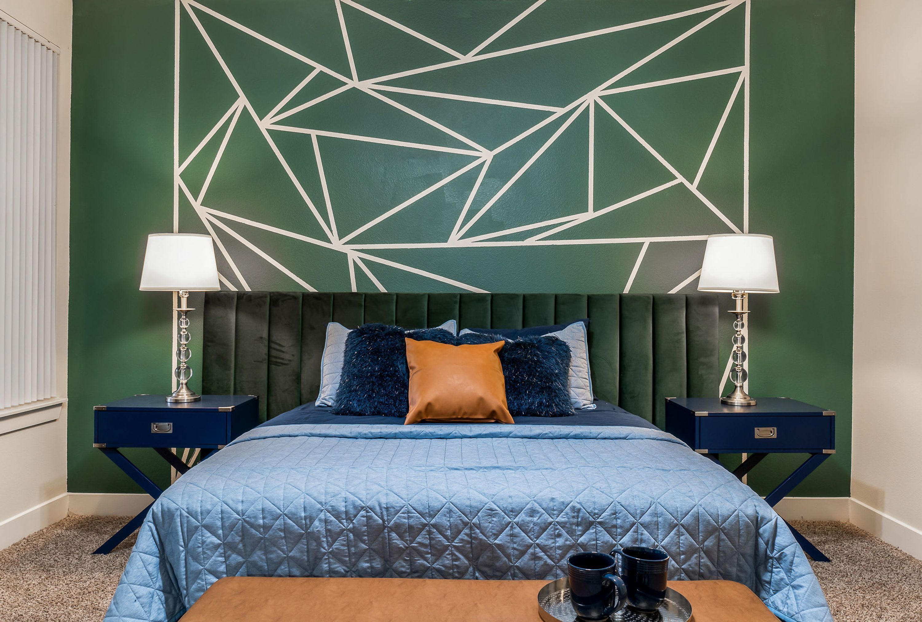 Un letto rifatto con copriletto blu, due comodini con lampade e un motivo geometrico sulla parete.