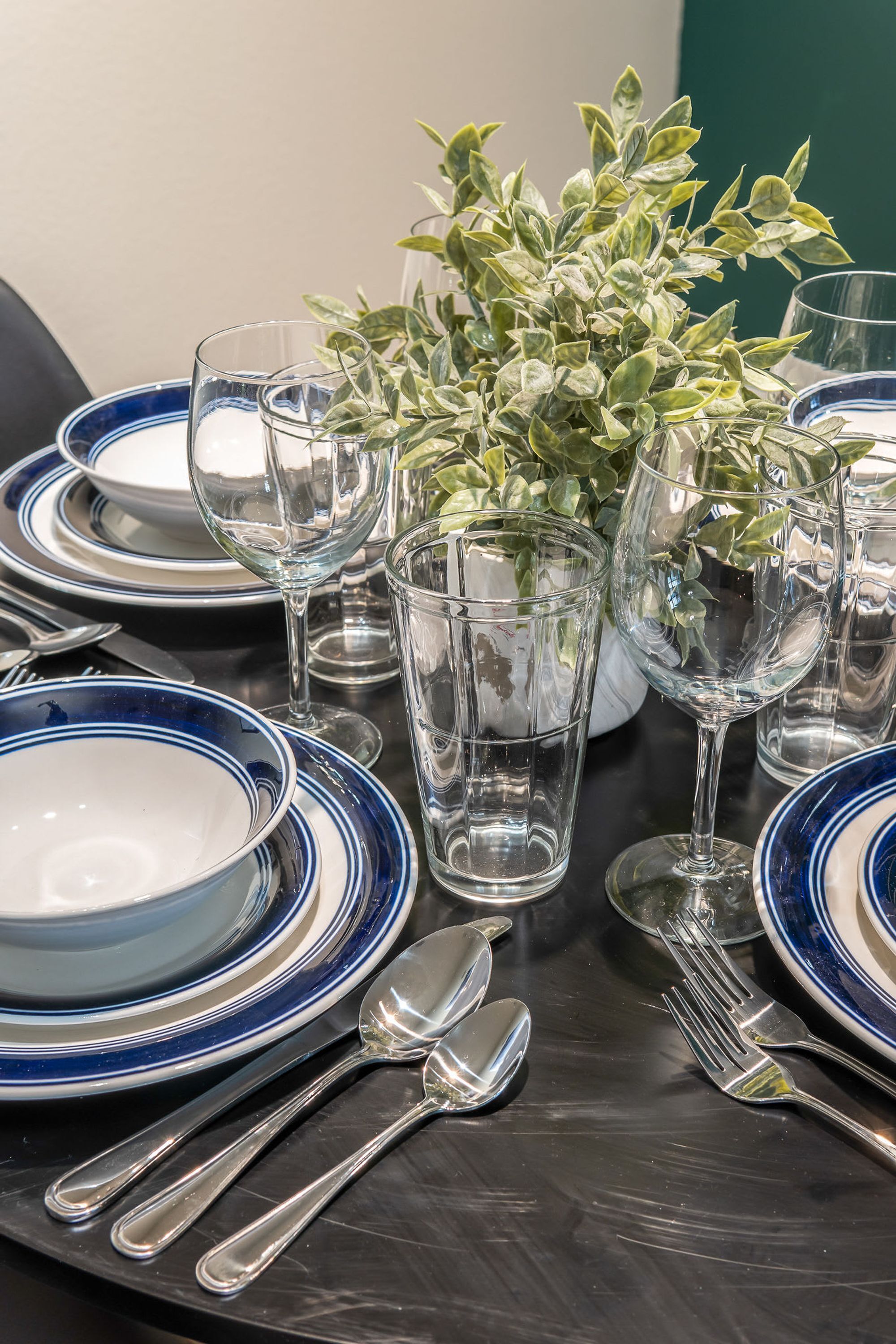 A table set with blue and white plates, clear glasses, and silverware, accompanied by a potted plant.