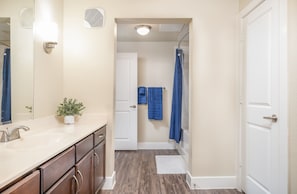 A bathroom with a white sink, wooden cabinets, a potted plant, and a shower with a blue curtain. - Kaleidoscope Near Galleria Medical City (Dallas)