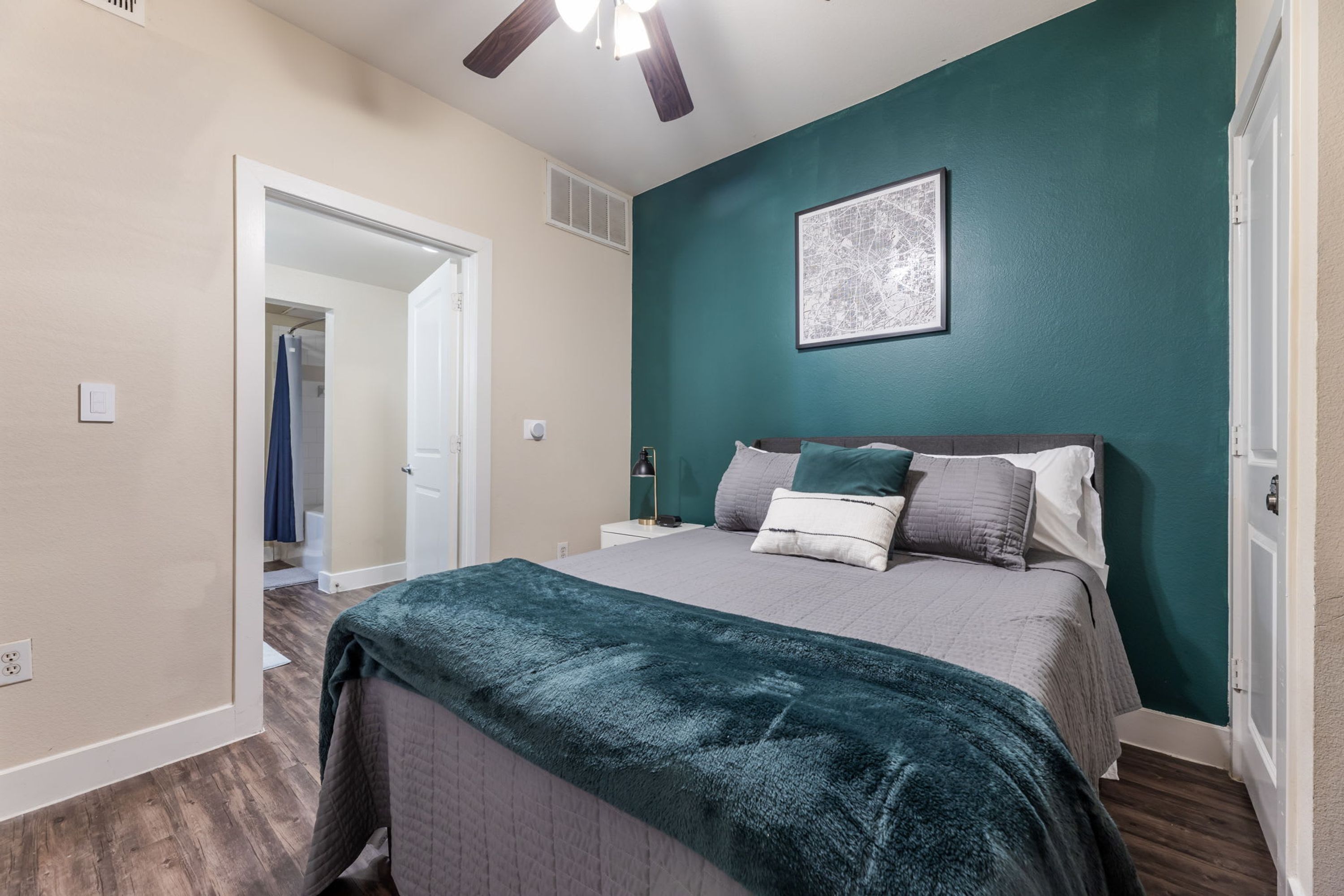 Une chambre à coucher comprenant un lit, un ventilateur de plafond, une table de chevet et une porte donnant sur une autre pièce.
