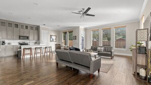 A spacious living area with a kitchen, a grey sofa, a dining table, and a ceiling fan. - Trinity Groves Retreat Large Modern 5 BR Home (Dallas)