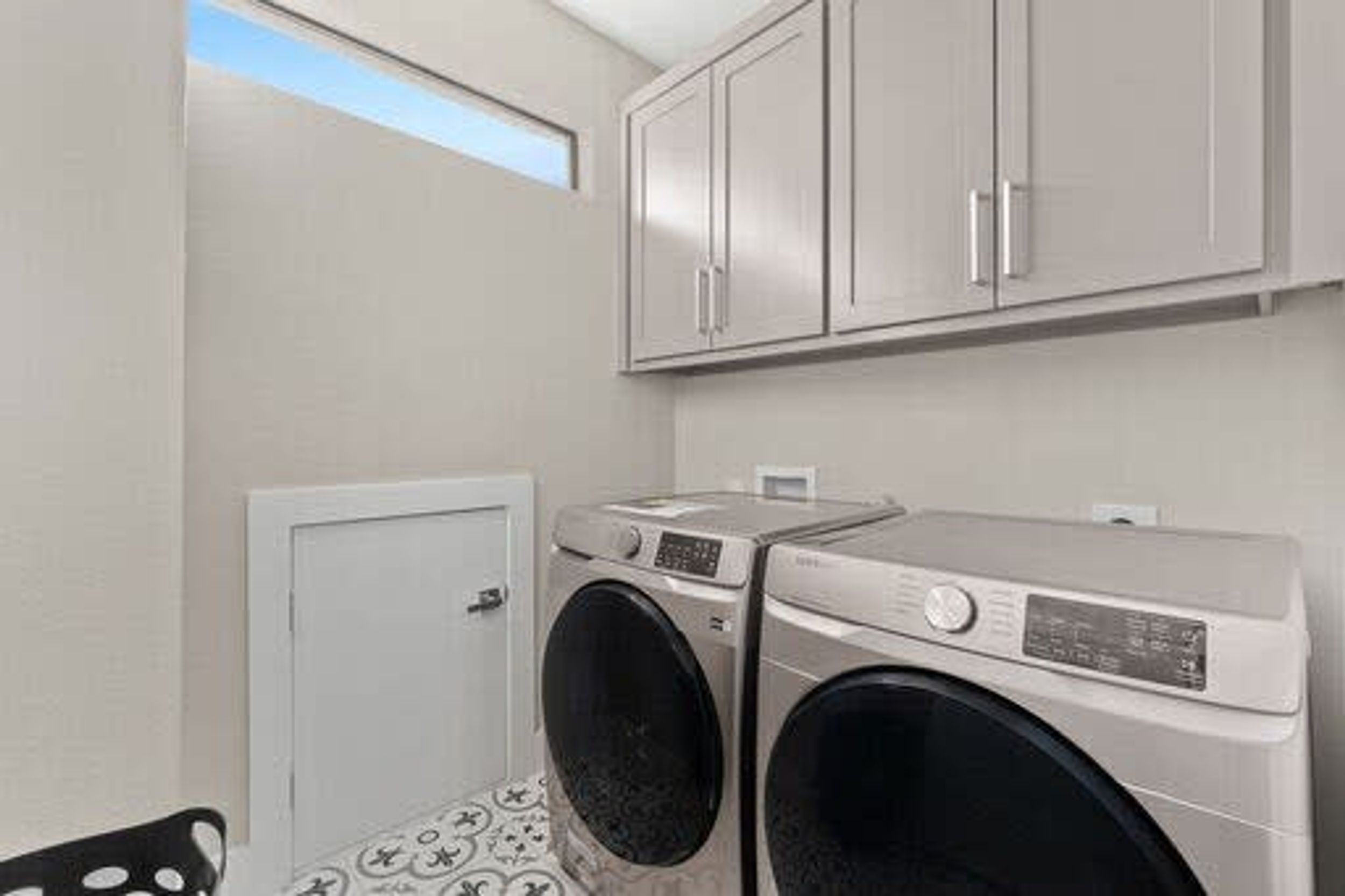 A compact laundry room with two front-loading washing machines, a small cabinet above, and a door to the left.