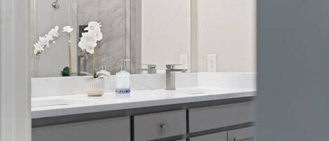 A bathroom with a large mirror, white sink, and grey cabinets.