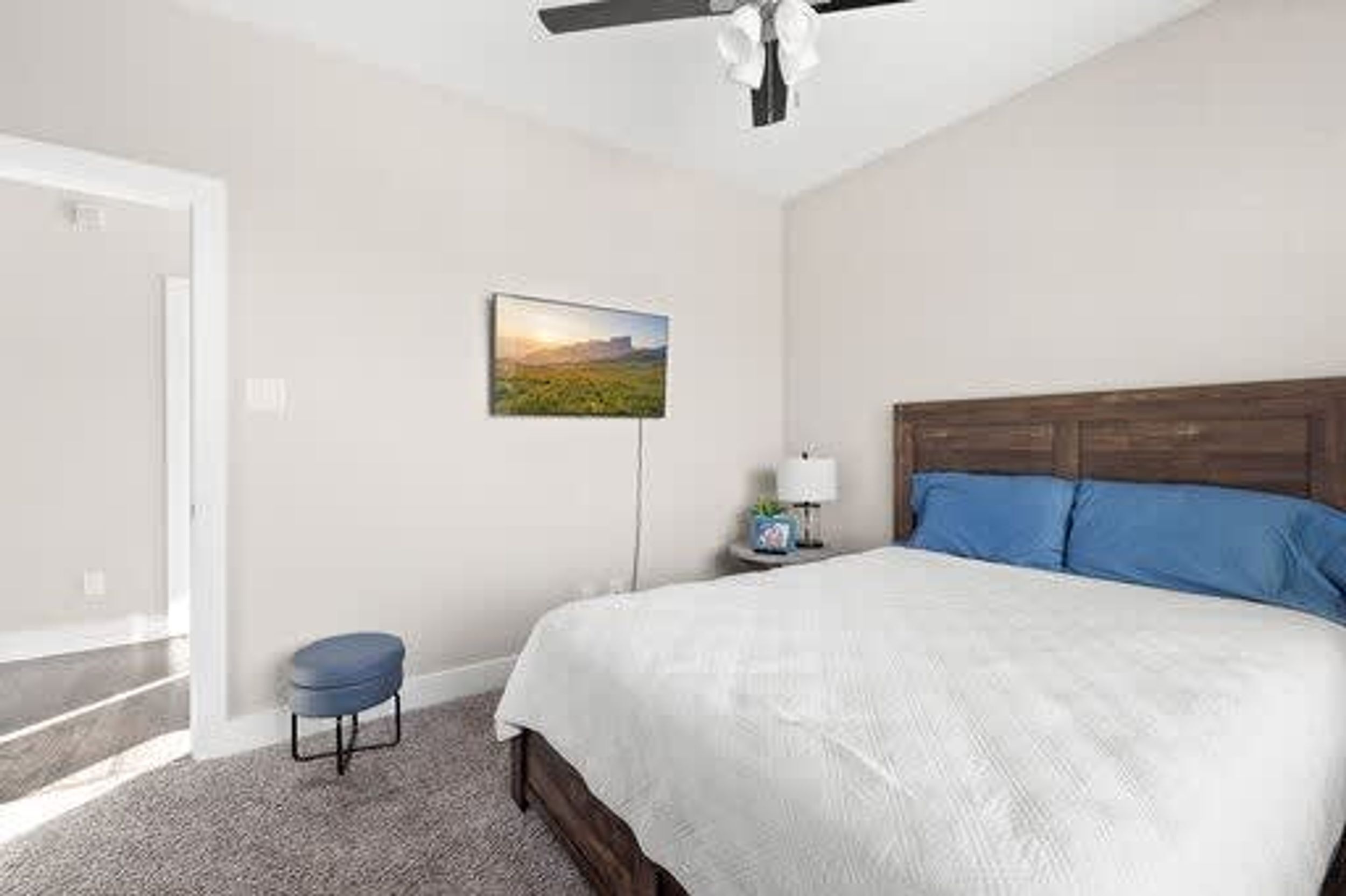 A bedroom with a bed, a nightstand, a lamp, a ceiling fan, a window, and a painting on the wall.
