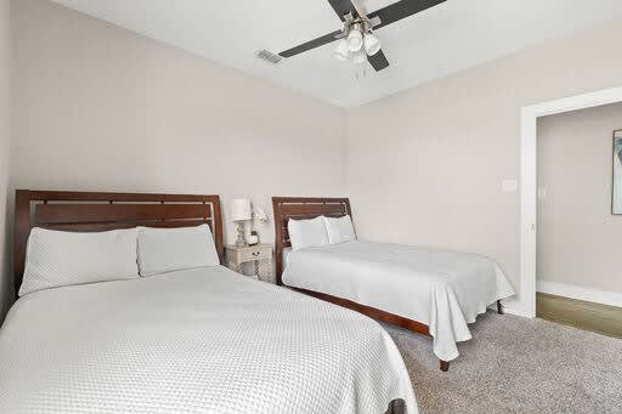 A hotel room with two single beds, a ceiling fan, and a nightstand with a lamp.