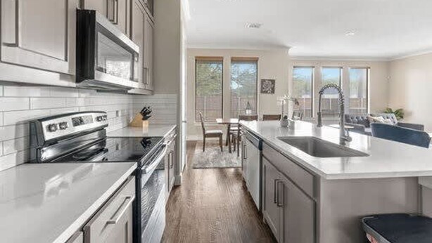 A modern kitchen with stainless steel appliances, a large island with a sink, and a dining area with a view. - Trinity Groves Retreat Large Modern 5 BR Home (Dallas)