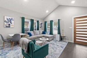 A modern living room with a sectional sofa, a dining table, and a green armchair. - Emerald Indigo House Pet Friendly (Dallas)