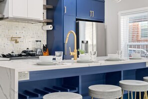 A modern kitchen with a central island, blue cabinets, and bar stools. - Emerald Indigo House Pet Friendly (Dallas)