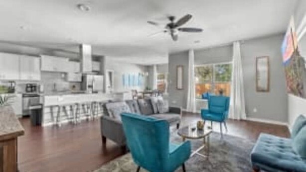 A spacious living area with a large sofa, a coffee table, and two blue armchairs. There is a kitchen in the background with white cabinets and a bar area. - Large 3BD 2BR Lower Bishop Arts Near Downtown Dallas (Dallas)