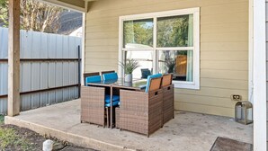 A covered patio with a wicker table and chairs, a window, and a metal fence in the background. - Large 3BD 2BR Lower Bishop Arts Near Downtown Dallas (Dallas)