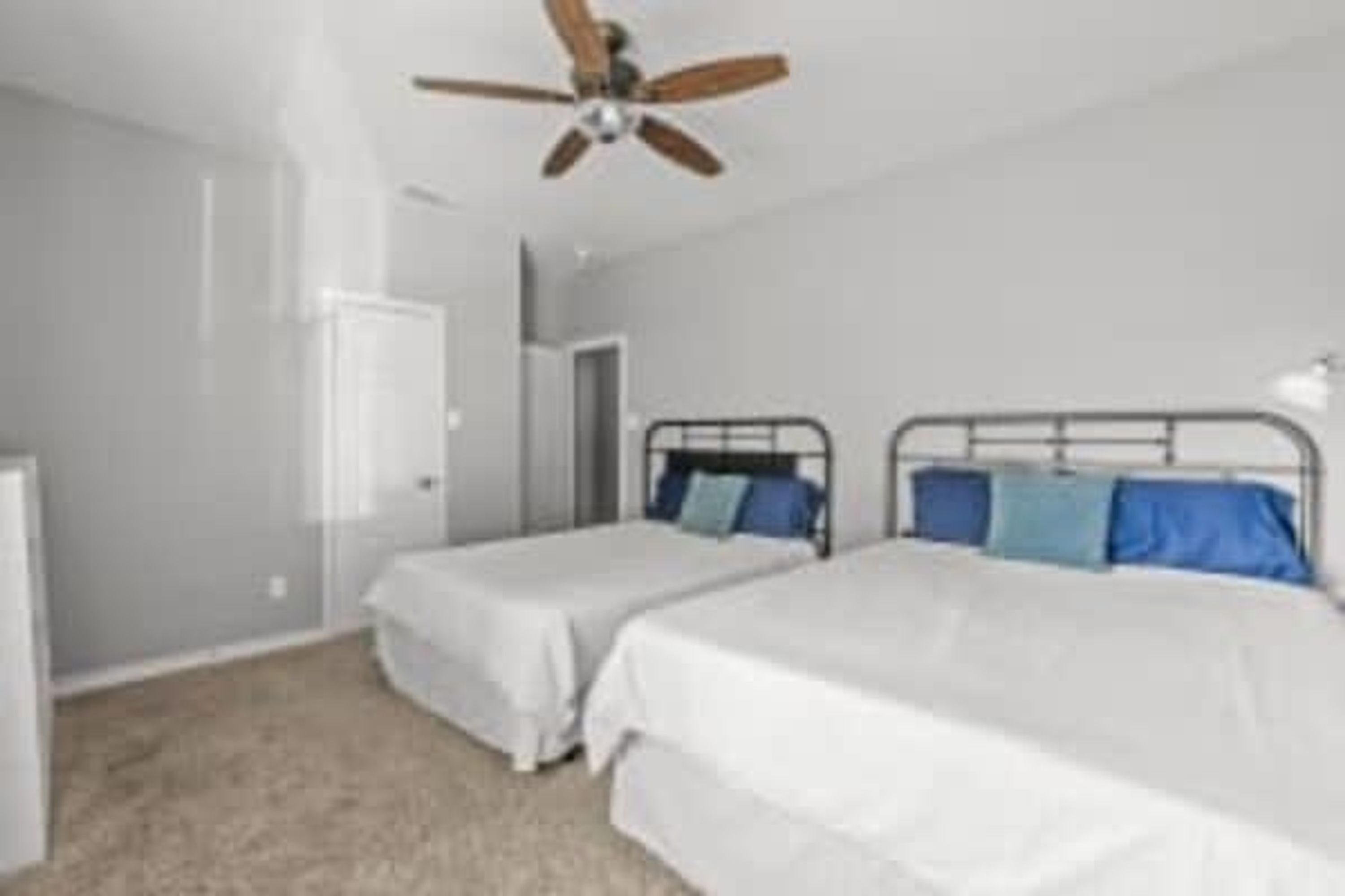 A bedroom with two single beds, a ceiling fan, and a door leading to another room.