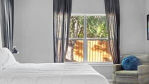 A bedroom with a large bed, a chair, and a window with curtains. - Large 3BD 2BR Lower Bishop Arts Near Downtown Dallas (Dallas)