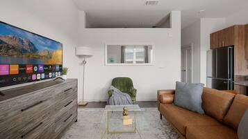Uma sala de estar moderna com televisão de tela plana, um armário de madeira, um sofá de couro marrom, uma mesa de centro de vidro e uma poltrona verde.