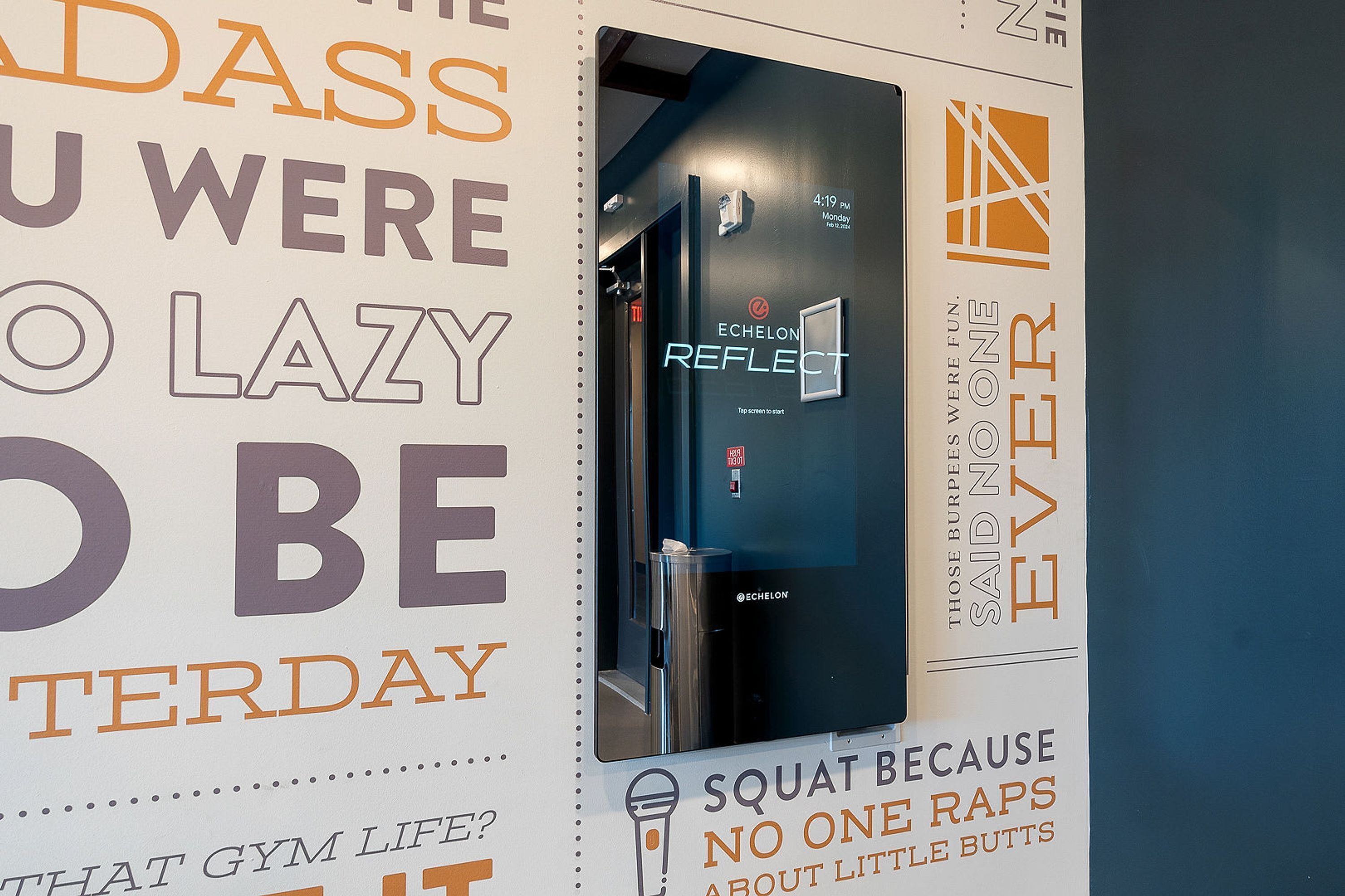 A gym wall with motivational posters and a mirror.