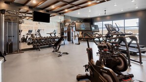 A gym with various exercise equipment, a large mirror, and a television screen.