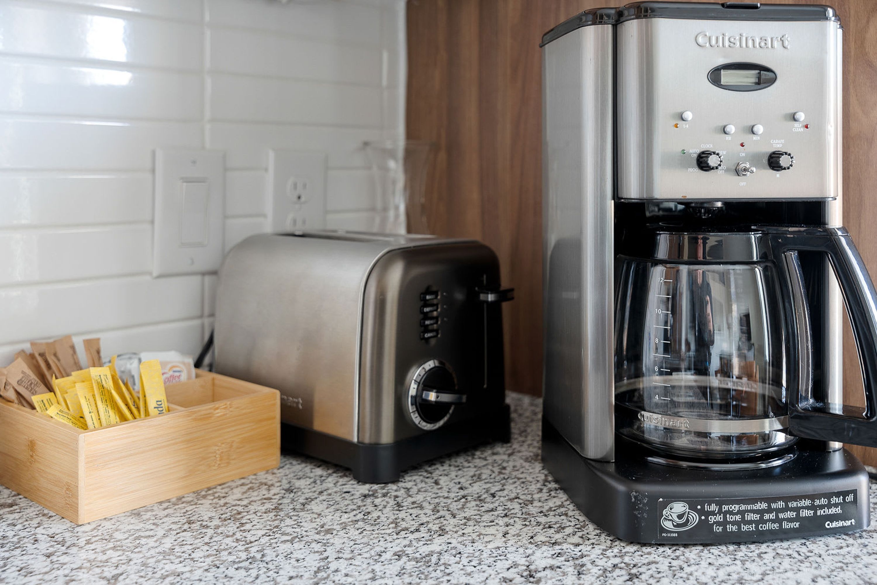 A kitchen with a Cuisinart coffee maker, a toaster, and a wooden box containing coffee pods.