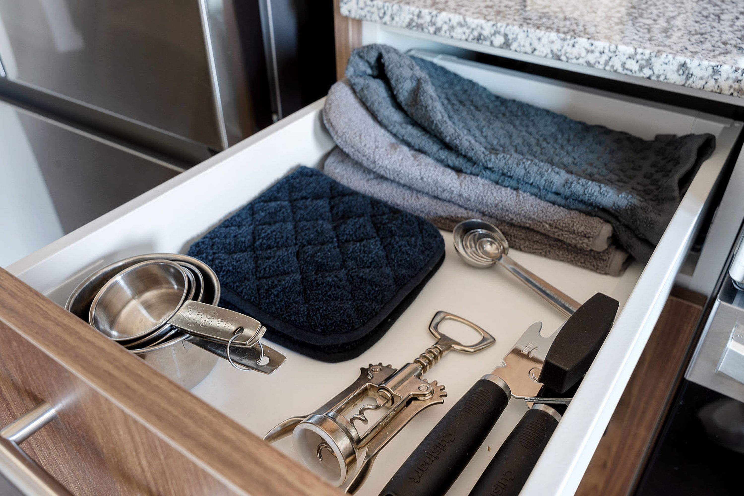 A drawer containing kitchen utensils, including a corkscrew, a measuring cup, and a knife set.