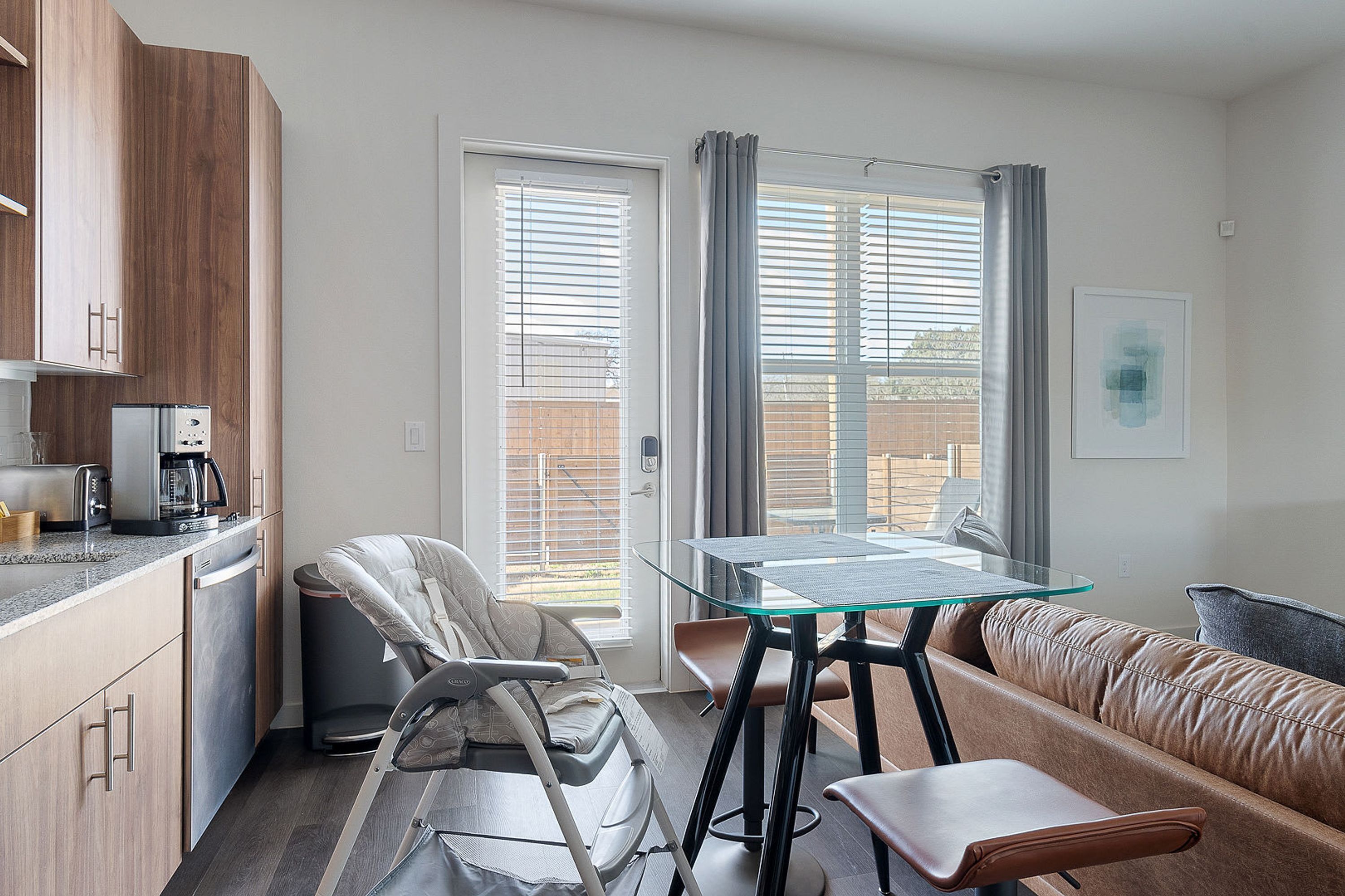 A compact kitchen with modern appliances, a dining area with a glass table, and a seating area with a sofa and chairs.