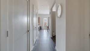A narrow hallway with white doors on one side and a wall-mounted mirror on the other.