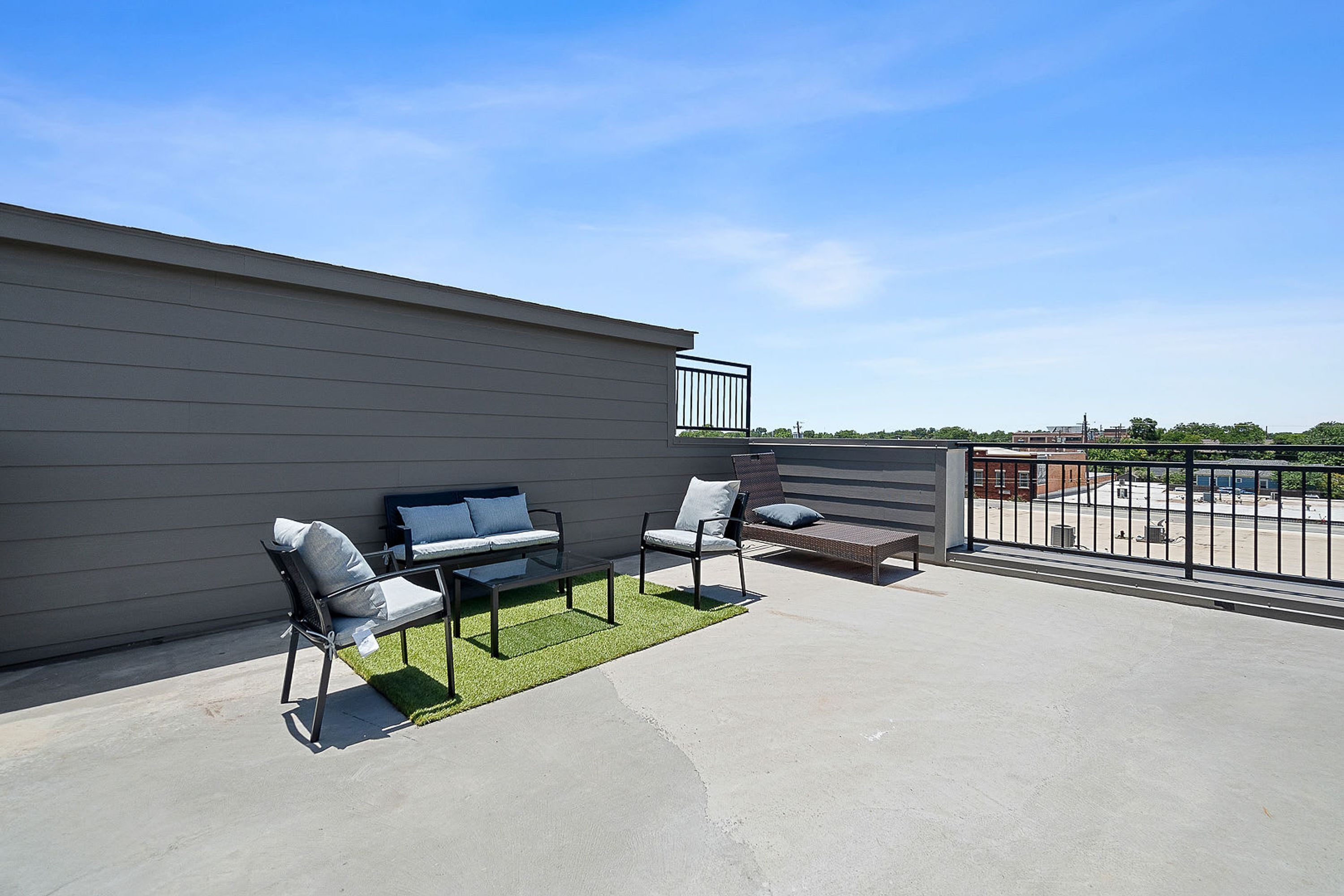 A rooftop patio with a concrete floor, two chairs, a small table, and a sofa.