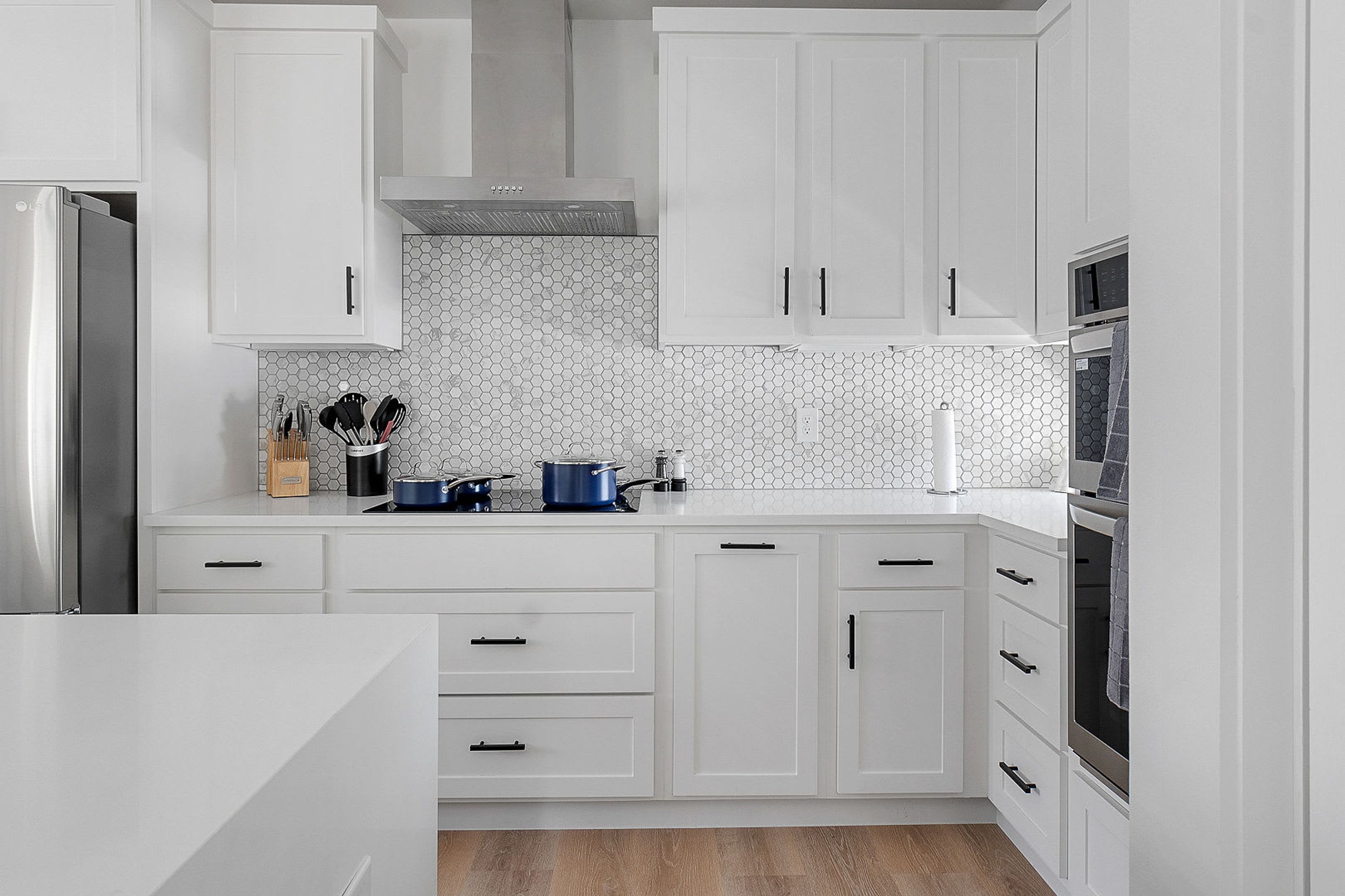 A modern kitchen with white cabinetry, a hexagonal backsplash, and stainless steel appliances.