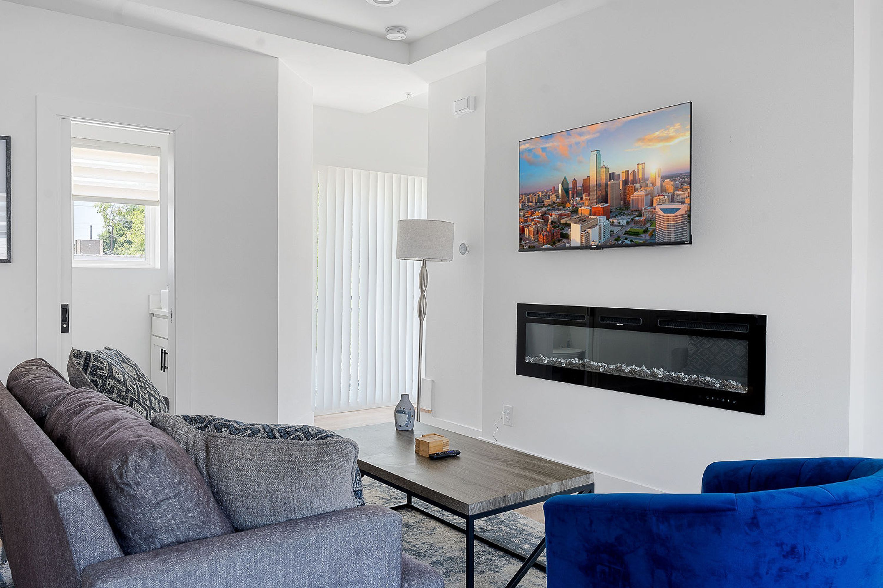 Ein modernes Wohnzimmer mit grauem Sofa, blauem Sessel, Couchtisch aus Holz und einem Stadtbild an der Wand.
