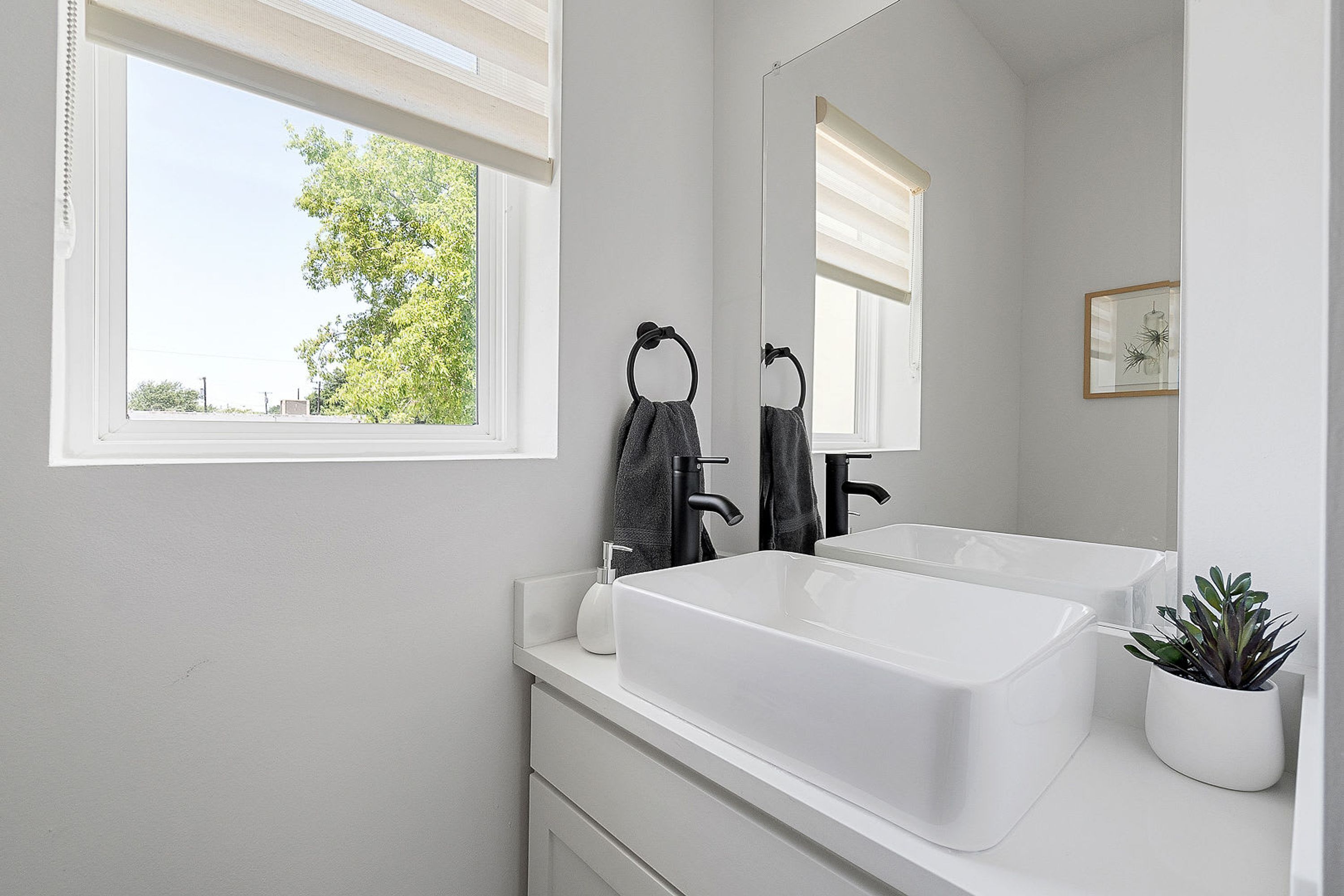 A bathroom with a large window, a white sink, and a mirror.