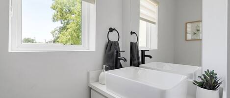 A bathroom with a large window, a white sink, and a mirror.