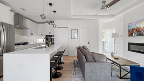 A modern kitchen with a central island, bar stools, and a dining area with a sofa and table.
