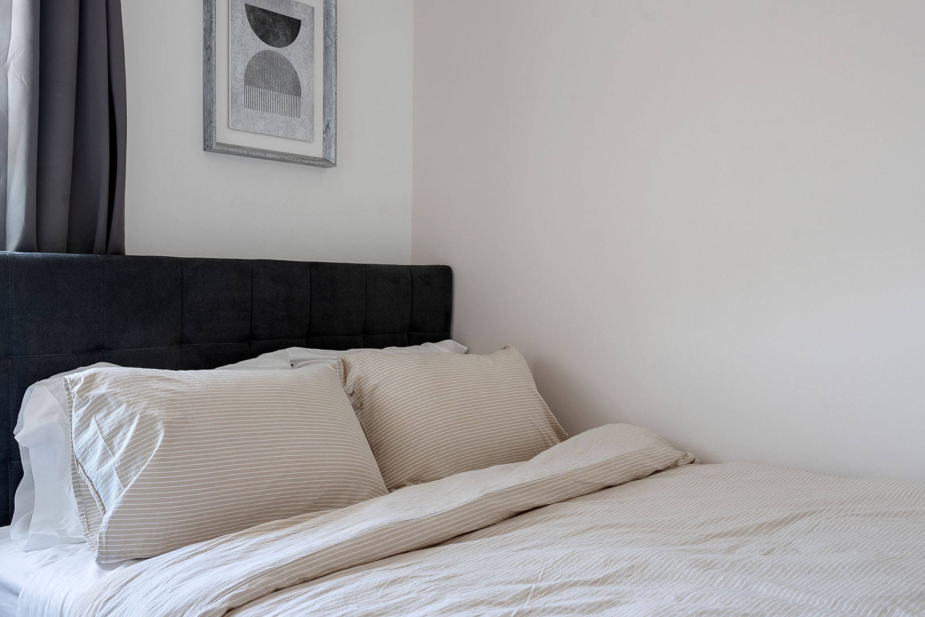Un lit bien fait, avec une tête de lit sombre, une literie blanche et un tableau encadré accroché au mur.