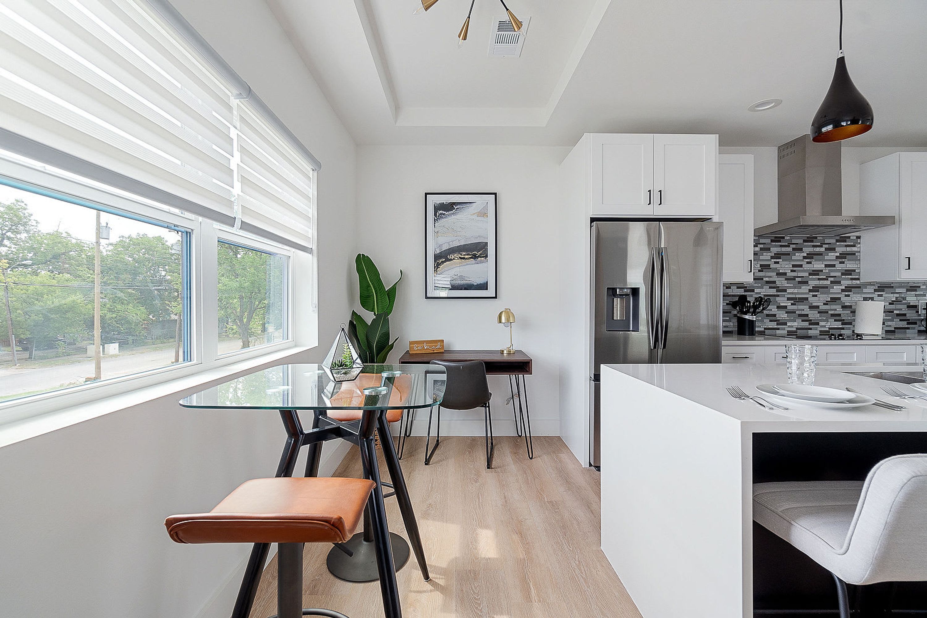 A modern kitchen with white cabinets, a stainless steel refrigerator, and a dining area with a glass table and chairs.