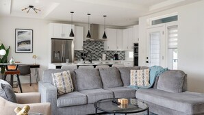 A modern living room with a grey sectional sofa, a glass coffee table, and a dining area with a white table and chairs. - Urban Comfort King Bed Rooftop Backyard (Dallas)