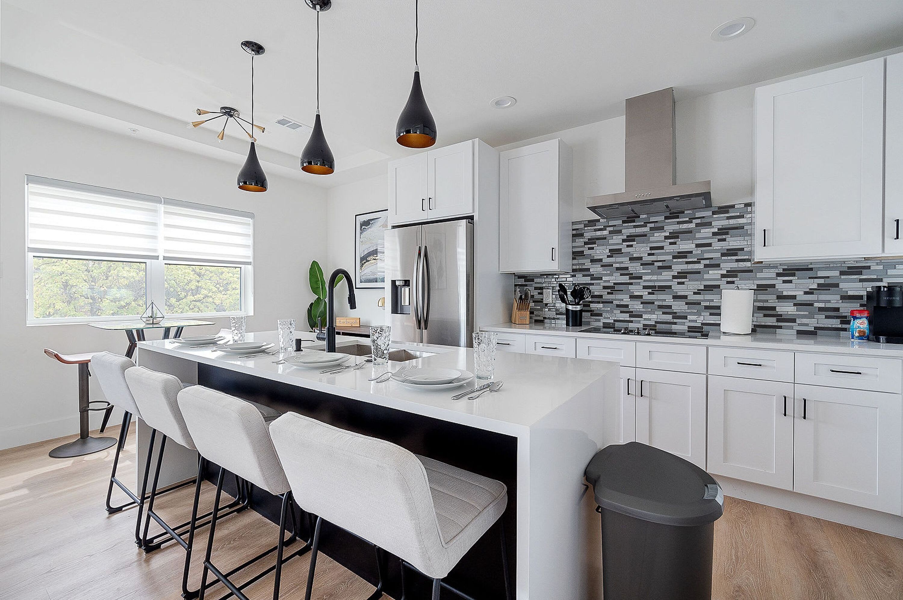 Una cocina moderna con armarios blancos, una isla grande con taburetes de bar e iluminación colgante.