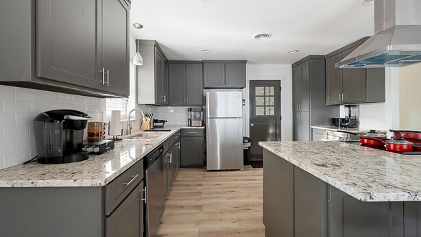 A modern kitchen with grey cabinets, stainless steel appliances, and a marble countertop.