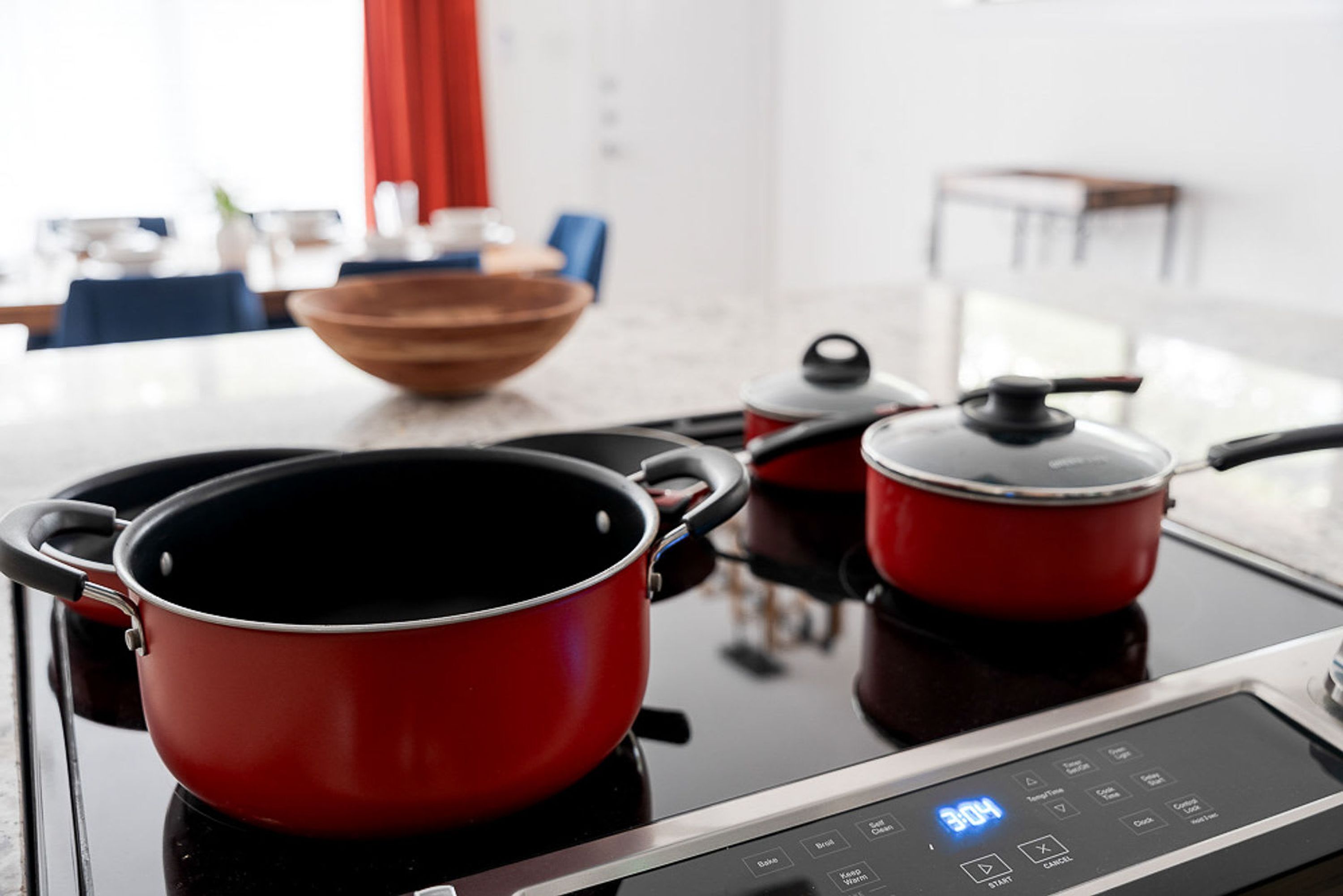 A kitchen with a stove, two red pots, and a wooden bowl on the counter.