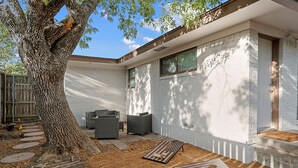 A modern house with a large tree, outdoor seating, and a brick wall.