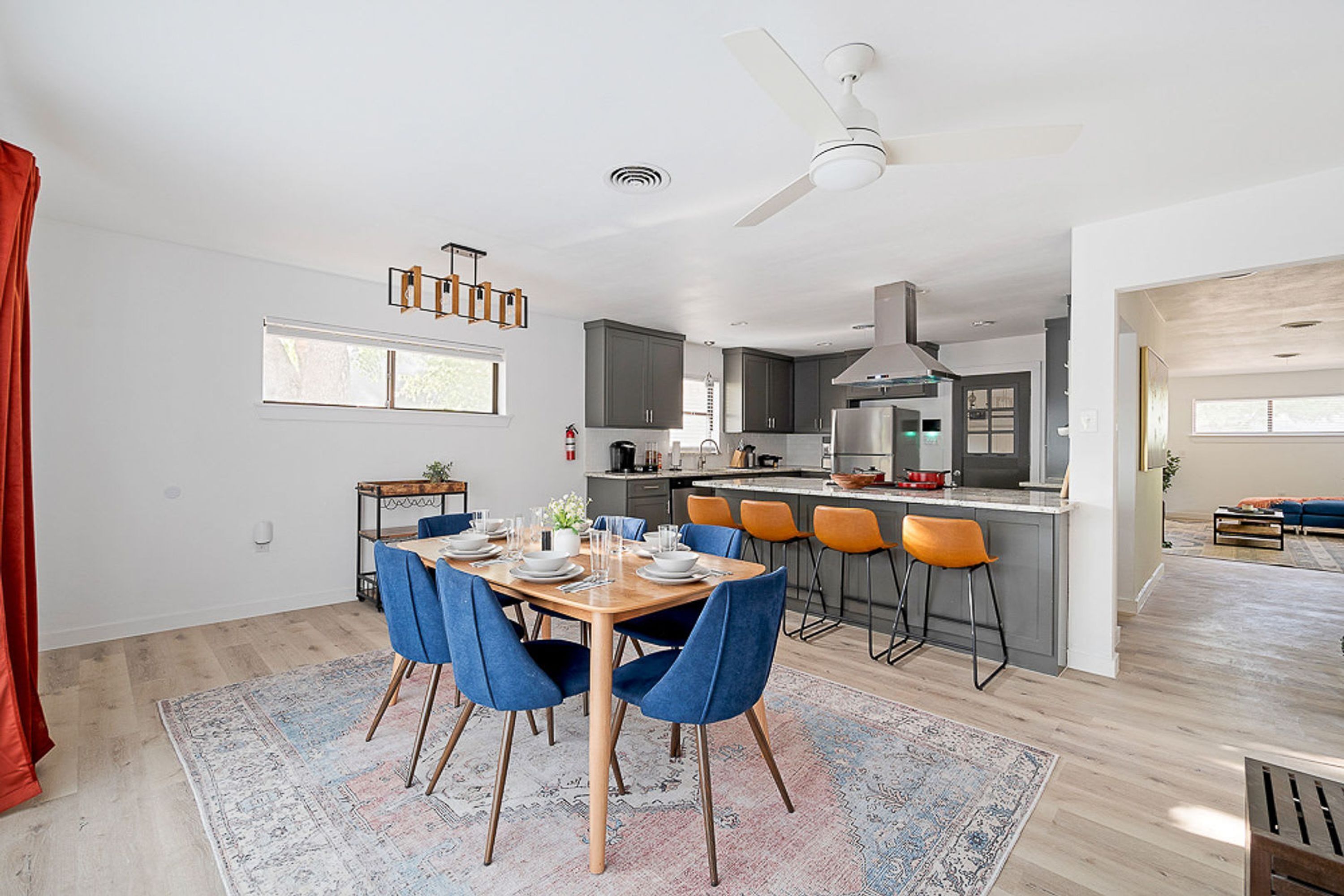 A modern kitchen with a central island, grey cabinets, and a dining area with blue chairs and a wooden table.