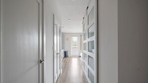 Un pasillo con puertas blancas y piso de madera que conduce a una puerta con ventanal.