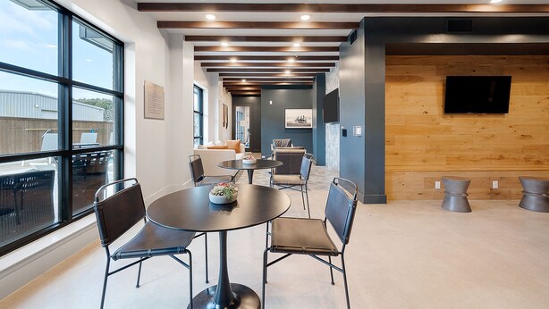 Un espacio de oficina moderno con mesas y sillas redondas, ventanas amplias y una pared de acento de madera.