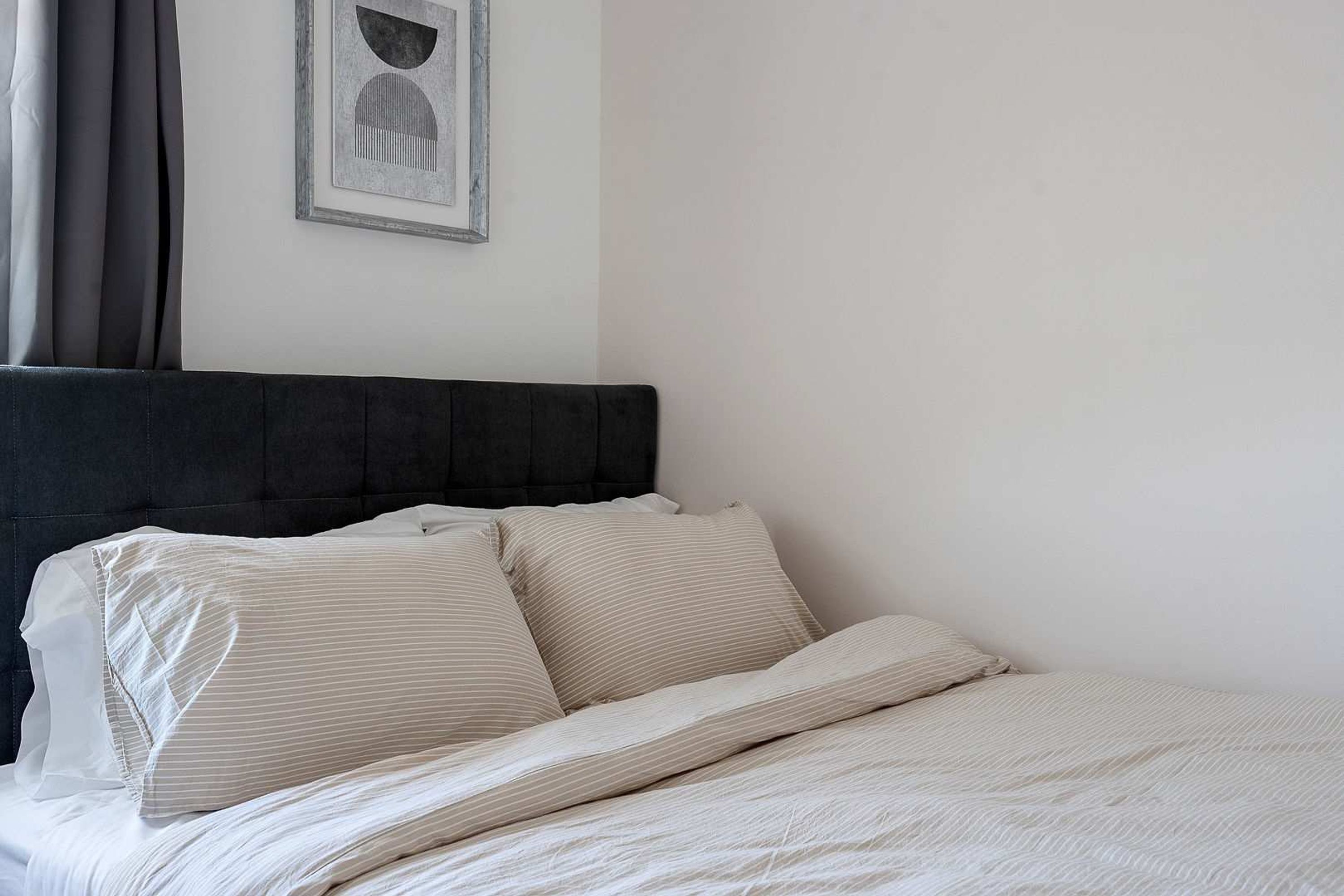 Una cama bien hecha con cabecera oscura y ropa de cama en tonos claros en una habitación sencilla y limpia.