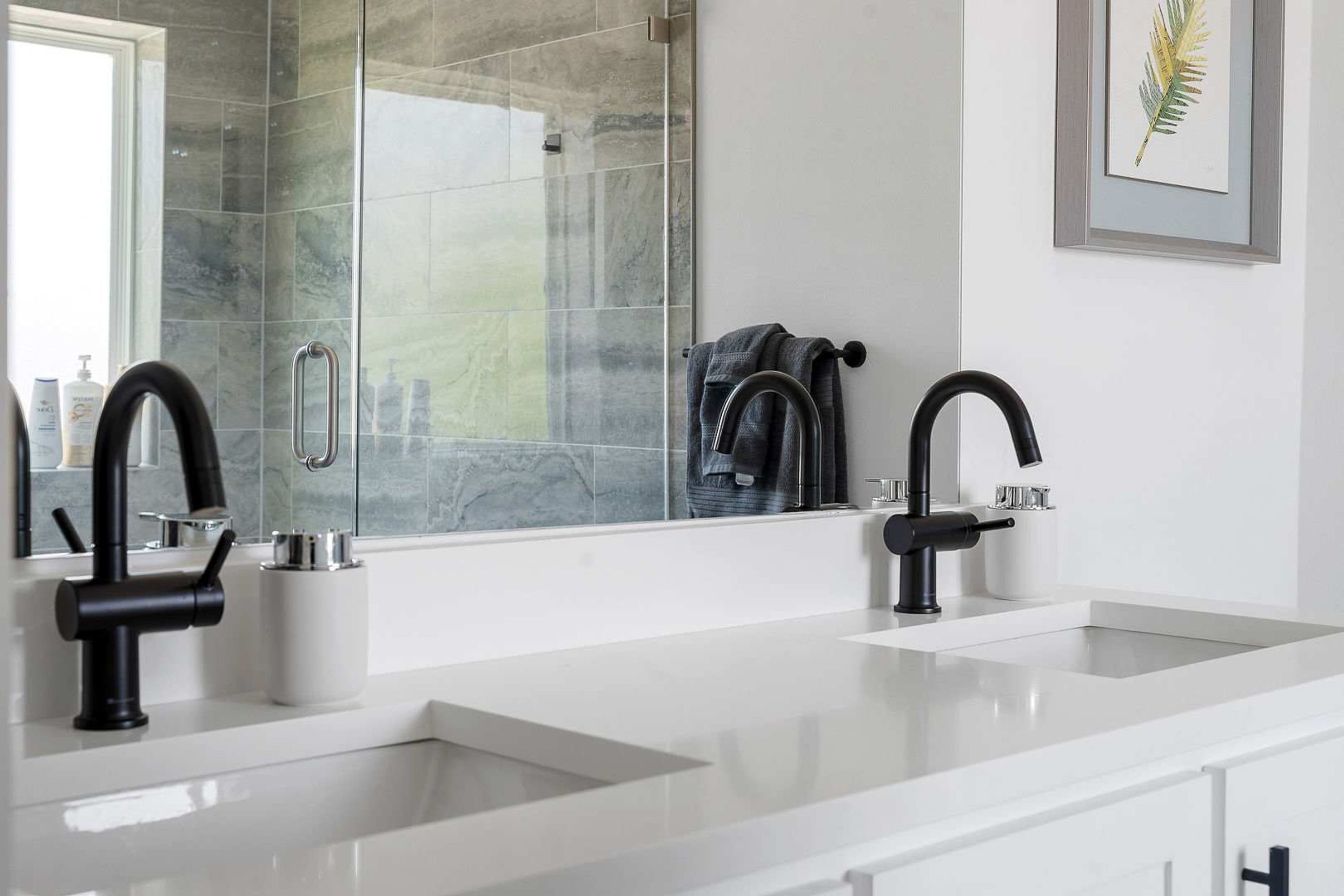 A modern bathroom with two sinks, a large mirror, and a framed plant on the wall.